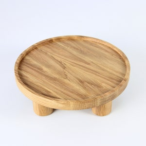 May include: A round wooden tray with three legs. The tray is made of light brown wood and has a smooth surface.