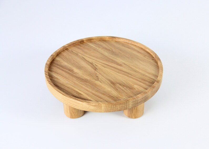 May include: A round wooden tray with three legs. The tray is made of light brown wood and has a smooth surface.