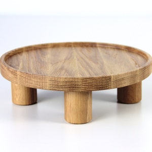 May include: A round wooden tray with four legs. The tray is made of light brown wood and has a smooth surface.