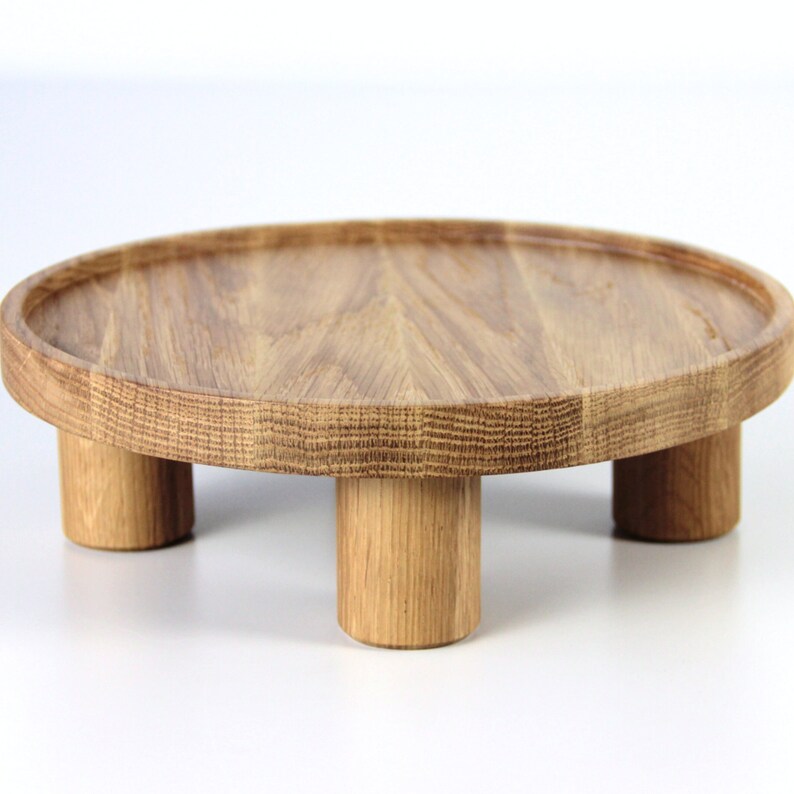 May include: A round wooden tray with four legs. The tray is made of light brown wood and has a smooth surface.
