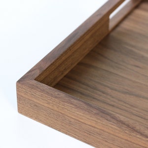Puede incluir: Una bandeja rectangular de madera con un acabado de madera natural y un asa recortada. La bandeja est&aacute; hecha de madera maciza y tiene una superficie lisa.