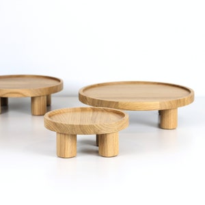 May include: Three wooden round display stands of varying sizes with four legs each. The stands are made of natural wood and are arranged in a row from largest to smallest.