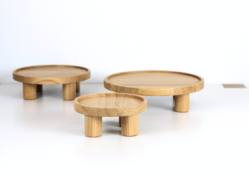 May include: Three wooden round display stands of varying sizes with four legs each. The stands are made of natural wood and are arranged in a row from largest to smallest.