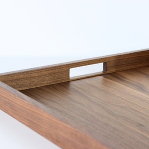 Puede incluir: Una bandeja rectangular de madera con acabado en nogal marr&oacute;n. La bandeja tiene un asa integrada con un recorte rectangular.