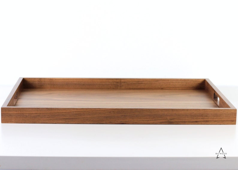 Puede incluir: Una bandeja rectangular de madera con un acabado de madera natural. La bandeja tiene un borde elevado y dos peque&ntilde;as asas recortadas en los lados.