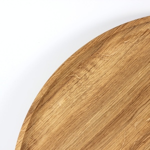 Close-up of a round oak wood serving tray showing natural wood grain patterns and smooth finish.