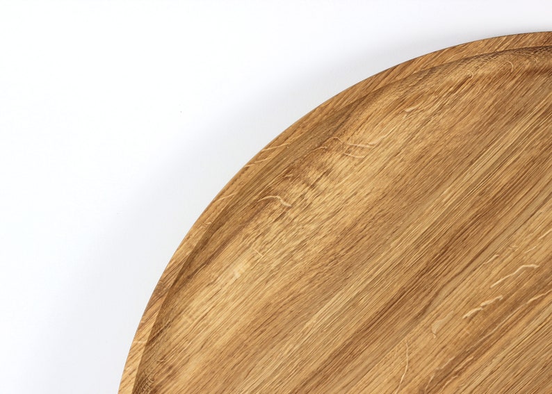 Close-up of a round oak wood serving tray showing natural wood grain patterns and smooth finish.