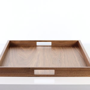 Puede incluir: Una bandeja rectangular de madera para servir con dos asas recortadas a cada lado. La bandeja est&aacute; hecha de madera de nogal y tiene un acabado natural.