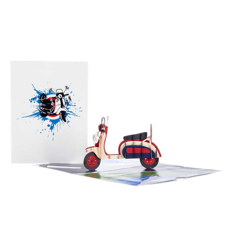 Puede incluir: Una tarjeta emergente roja, blanca y azul con un scooter vintage. La tarjeta est&aacute; abierta y el scooter est&aacute; en primer plano. El fondo de la tarjeta presenta un dise&ntilde;o de salpicaduras azul y blanco con una silueta negra y blanca de un scooter.