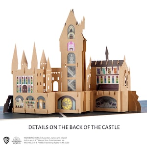 May include: A tan cardboard pop-up castle structure featuring multiple towers, arched windows, and detailed interior illustrations including potion bottles, staircases, and a circular emblem. The text "DETAILS ON THE BACK OF THE CASTLE" appears below.