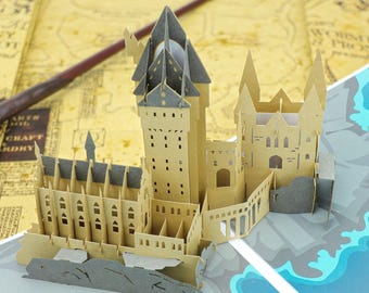 May include: A three-dimensional paper craft model of a castle featuring tan walls, grey roofs, and intricate architectural details including arched windows and tall towers. The structure is constructed from layered cardstock with cutouts.