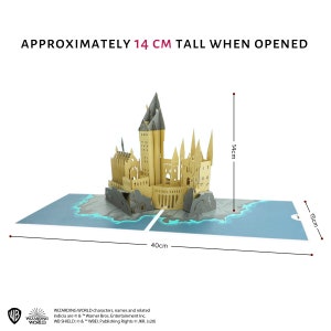 May include: A tan paper pop-up castle model featuring multiple towers and spires, set on a blue base with rocky details. The structure measures 14 cm tall when opened, with a total base width of 40 cm and a depth of 15 cm, including Wizarding World text.