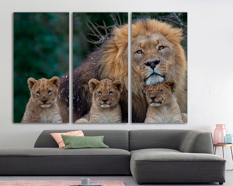 May include: A large male lion with a thick mane is surrounded by three young cubs. The lion is looking directly at the camera, while the cubs are looking at the lion. The background is a blurred green forest.
