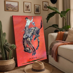 May include: A large, rectangular canvas print featuring a rodeo scene with a cowboy on a bucking bronco against a vibrant red background. The print includes the text "LET 'ER BUCK" and is accompanied by a tan cowboy hat on the floor.