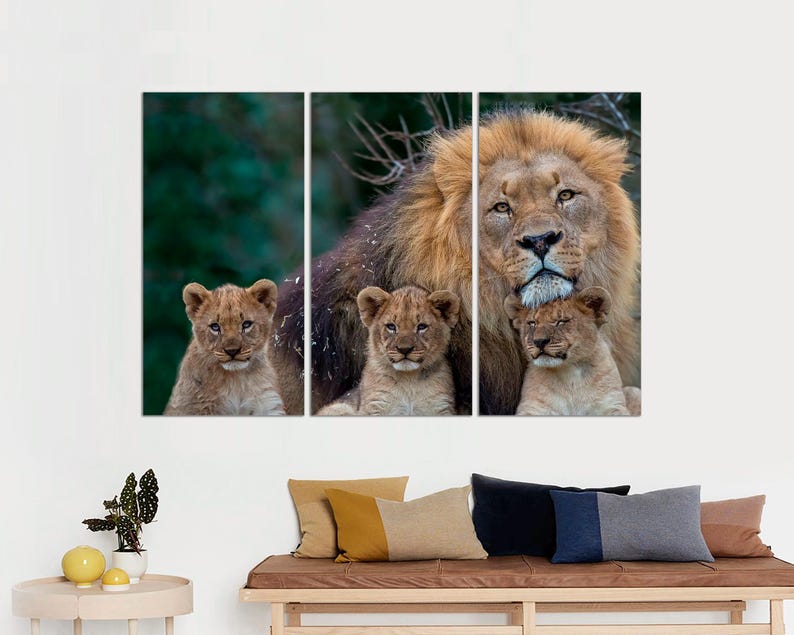 May include: A large male lion with a thick mane is surrounded by three cubs. The lion is looking directly at the camera, while the cubs are looking at the lion. The background is a blurred green forest.