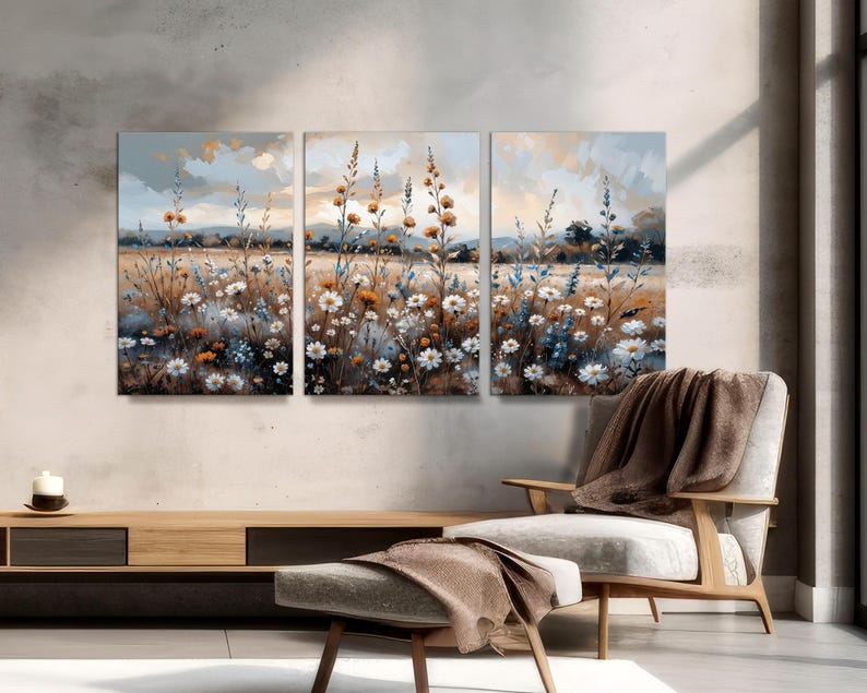 Op de afbeelding: Een driedelig canvas kunstwerk dat een veld met wilde bloemen in aquarel stijl toont. Het kunstwerk toont witte, blauwe en oranje bloemen met een zacht, gedempt kleurenpalet. De achtergrond toont een landschap met een bewolkte lucht.