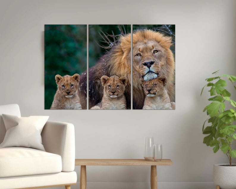 May include: A large male lion with a thick mane stands with three cubs. The lion is looking directly at the camera. The cubs are nestled against the lion's body. The background is a blurred green forest.