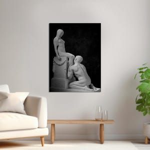 May include: Black and white photograph of two statues, one sitting on a pedestal and the other kneeling. The statues are in a romantic pose, with the kneeling statue looking up at the seated statue.