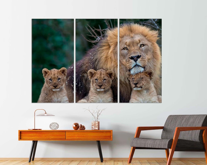 May include: A large male lion with a thick mane stands with two young cubs nestled against him. The lion is brown and has a light brown mane. The cubs are light brown with dark brown spots. The background is a blurred green forest.