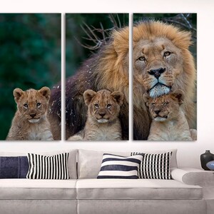 May include: A large male lion with a thick mane is surrounded by three cubs. The lion is looking directly at the camera, while the cubs are looking up at the lion. The background is a blurred green forest.