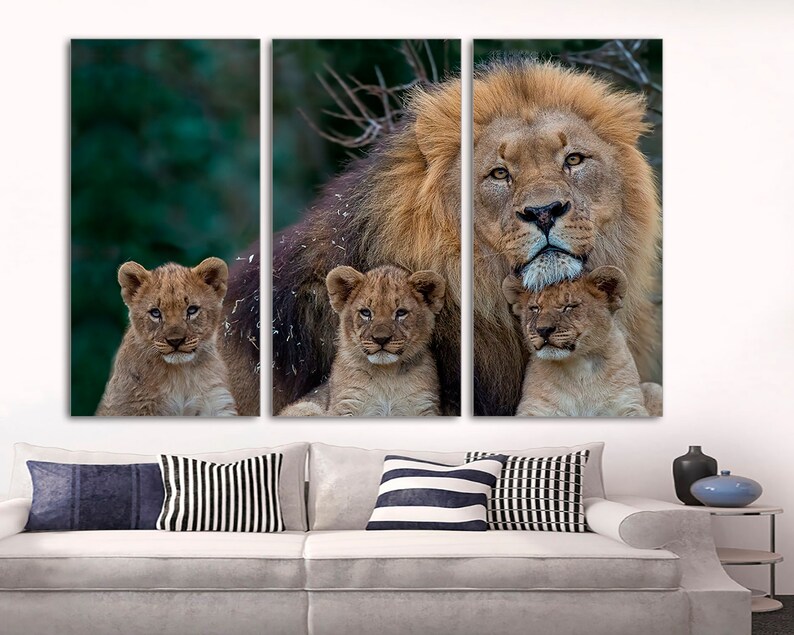 May include: A large male lion with a thick mane is surrounded by three cubs. The lion is looking directly at the camera, while the cubs are looking up at the lion. The background is a blurred green forest.