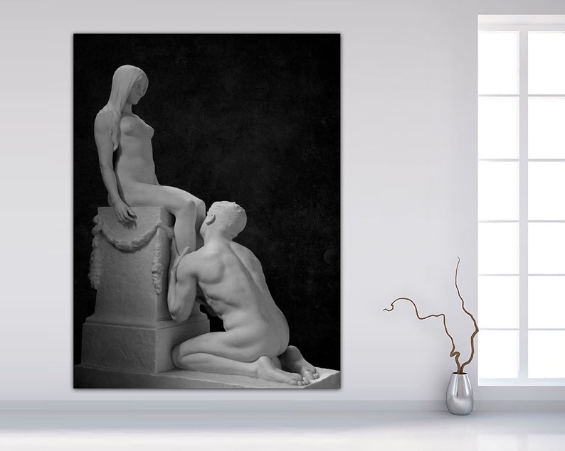 May include: Black and white photograph of a sculpture depicting a nude woman sitting on a pedestal with a man kneeling before her.