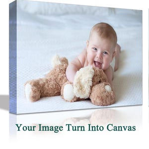 May include: A baby is lying on a white bedspread and smiling while holding a brown plush toy. The baby is wearing a white nappy and has a light brown complexion.
