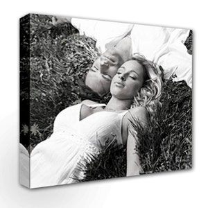 May include: A black and white photograph of a couple lying in a field of grass. The woman is wearing a white dress and has her eyes closed. The man is wearing a white shirt and has his eyes closed. The couple is lying close together, with their heads resting on each other's shoulders.