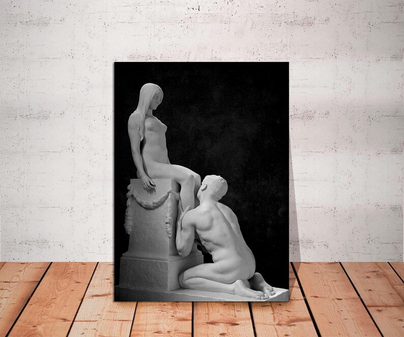 May include: Black and white photograph of two marble statues. The statues depict a woman sitting on a pedestal and a man kneeling before her.