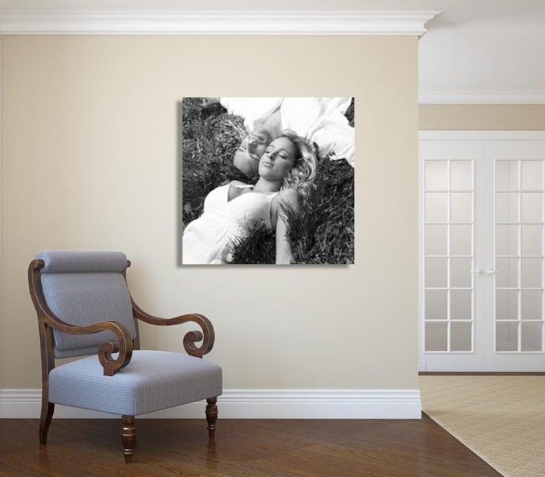 May include: A black and white photograph of a couple lying in a field of grass. The woman is wearing a white dress and has her eyes closed. The man is lying on his side with his head resting on her shoulder.