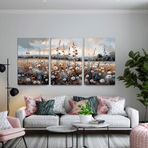 Op de afbeelding: Een drieluik van canvas kunst met een veld vol wilde bloemen in een zachte, impressionistische stijl. Het kunstwerk toont een sereen landschap met een gedempte kleurenpalet van blauw, bruin en wit, dat een gevoel van rust oproept.