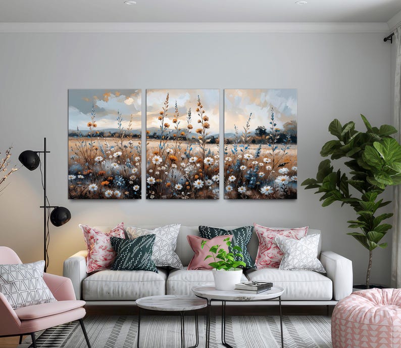 Op de afbeelding: Een drieluik van canvas kunst met een veld vol wilde bloemen in een zachte, impressionistische stijl. Het kunstwerk toont een sereen landschap met een gedempte kleurenpalet van blauw, bruin en wit, dat een gevoel van rust oproept.