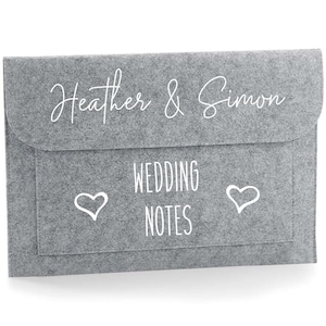 May include: Gray felt wedding planner folder with the text "Heather & Simon" and "Wedding Notes" with a heart on each side of the text.