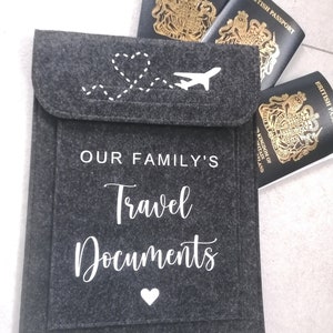 May include: Gray felt travel document holder with white stitching and the text "OUR FAMILY'S Travel Documents" and a white heart. Three British passports are visible on top of the holder.