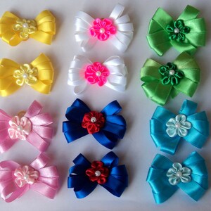 May include: Twelve handmade satin ribbon bows with pearl centers in various colors, including yellow, white, pink, blue, and green. The bows are arranged in three rows of four.