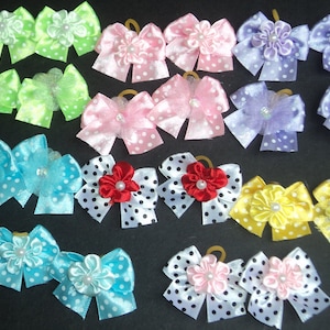 May include: Assortment of 18 handmade hair bows for pets. The bows are made of satin ribbon with polka dots and feature a variety of colors, including green, pink, purple, red, yellow, and blue. Each bow has a small flower accent in the center.