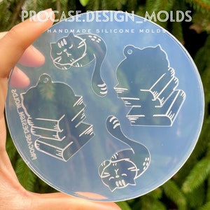 Peut inclure: Un moule en silicone transparent avec quatre motifs : un chat dormant sur une pile de livres, un chat assis sur une pile de livres, un chat enroulé dormant et une queue de chat. Le moule est étiqueté "Procase.Design_Molds Handmade Silicone Molds".