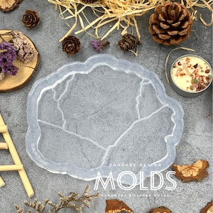 Pode incluir: Um molde de silicone transparente em forma de geodo com uma borda áspera e irregular. O molde está sobre uma superfície cinza com pinhas, flores secas e fatias de madeira. O texto "PROCASE DESIGN MOLDS HANDMADE SILICONE MOLDS" está impresso na superfície.