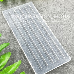 May include: A clear, rectangular silicone mold with vertical grooves. The mold has the text "PROCASE DESIGN MOLDS" and "HANDMADE SILICONE MOLDS" printed on it. The mold is designed for crafting and is shown on a gray surface.