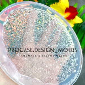 May include: A clear, round silicone mold with a textured surface filled with iridescent glitter. The text "PROCASE.DESIGN_MOLDS" and "HANDMADE SILICONE MOLDS" is printed on the mold. The mold is surrounded by colorful flowers.