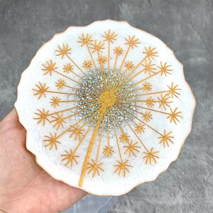 May include: White resin coaster with a gold glitter dandelion design. The dandelion has a gold stem and white petals with gold accents.