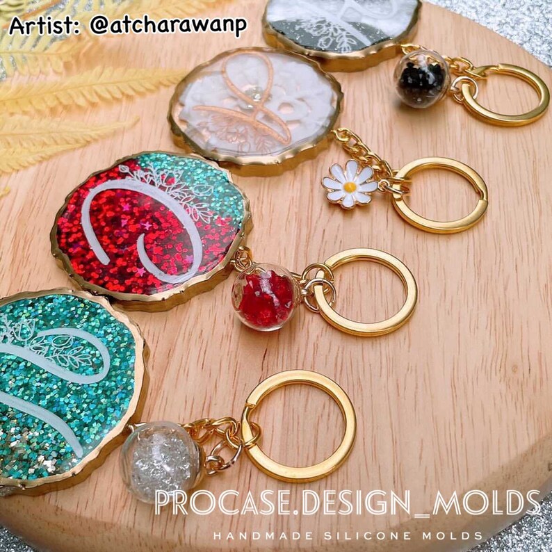 May include: A set of five resin keychains with gold accents. Each keychain features a different color and design, including red glitter, green glitter, white glitter, black glitter, and a white flower. The keychains are attached to gold rings and chains. The text "PROCASE.DESIGN_MOLDS" and "HANDMADE SILICONE MOLDS" is visible at the bottom of the image.