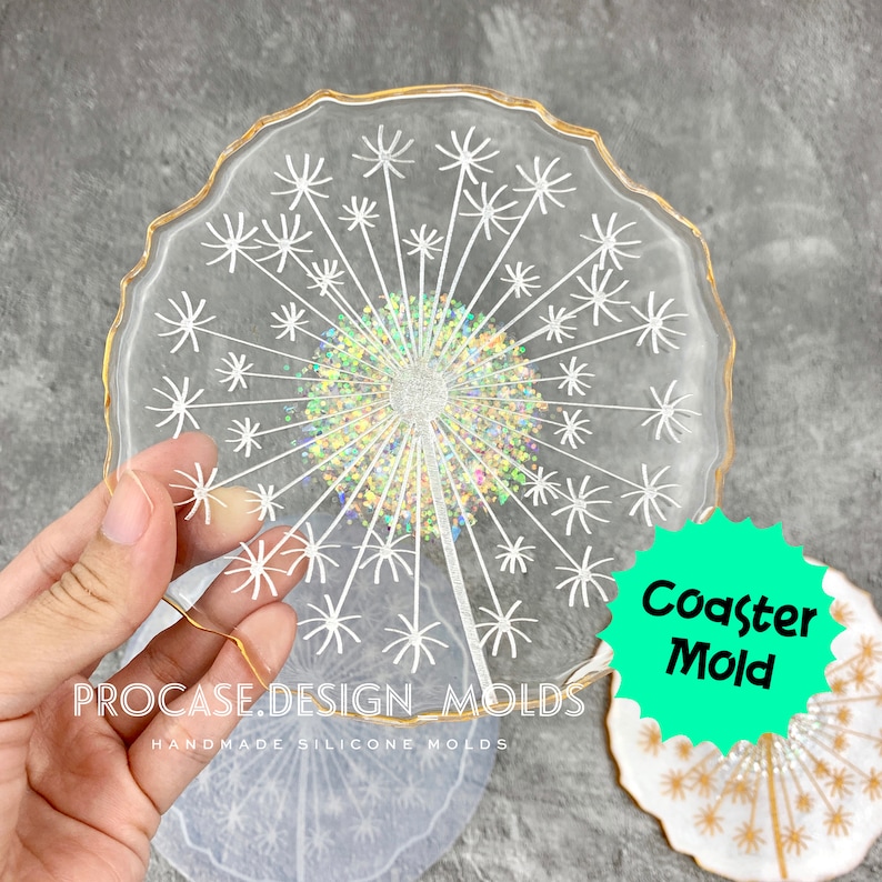 May include: A clear silicone mold shaped like a dandelion with a gold rim. The mold is designed to create a resin coaster. The text "Coaster Mold" is written on a green starburst sticker.