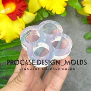 Puede incluir: Un molde de silicona transparente con cinco cavidades circulares, diseñado para crear artesanías de resina. El molde se sostiene en una mano, mostrando su tamaño y forma. El texto "PROCASE.DESIGN_MOLDS HANDMADE SILICONE MOLDS" es visible debajo del molde.