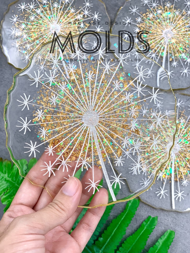 May include: A set of clear resin coasters with a gold glitter and white dandelion design. The coasters are handmade and have a slightly irregular shape. The text "PROCASE.DESIGN MOLDS HANDMADE SILICONE MOLDS" is visible in the image.