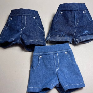 May include: Three pairs of denim shorts in different styles. The shorts are all blue and have a variety of stitching details.