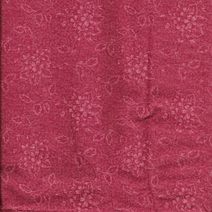 May include: A close-up of a red fabric with a white floral pattern. The fabric has a textured surface.