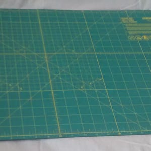 May include: A green self-healing cutting mat with a grid pattern and yellow lines. The mat has a ruler along the edges.