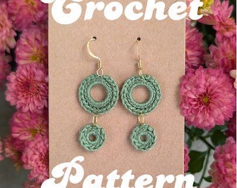 May include: A pair of sage green crochet earrings with gold-colored hooks and connectors. The earrings are circular, with a larger circle at the top and a smaller circle dangling below. The words "Crochet Pattern" are written in white script on a brown card.