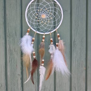 Könnte beinhalten: Weißer Traumfänger mit braunen und weißen Federn, die daran hängen. Der Traumfänger ist aus weißem Garn gefertigt und hat eine Holzkugel in der Mitte.